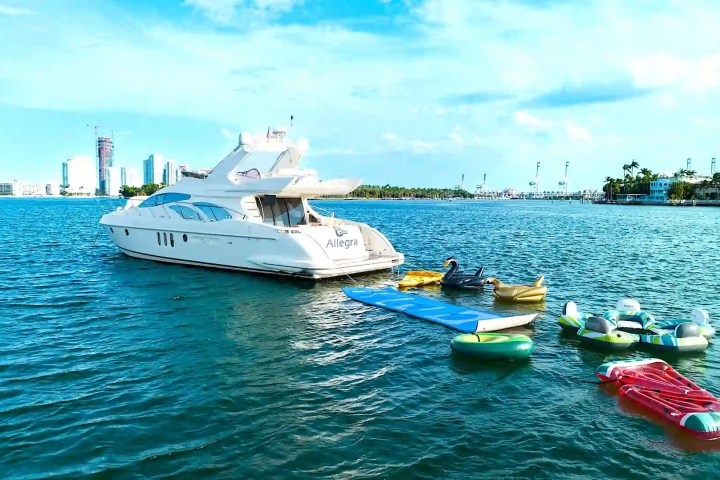 Yacht on water with inflatable floats nearby; city skyline background.