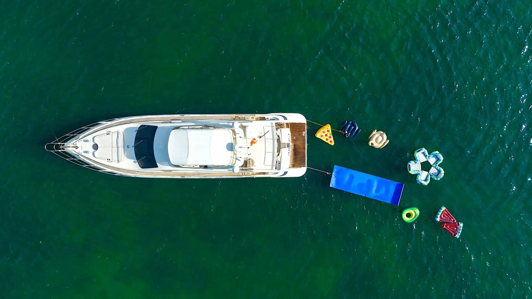 Aerial of 65′ Azimut yacht anchored with inflatable pool and floating toys behind stern