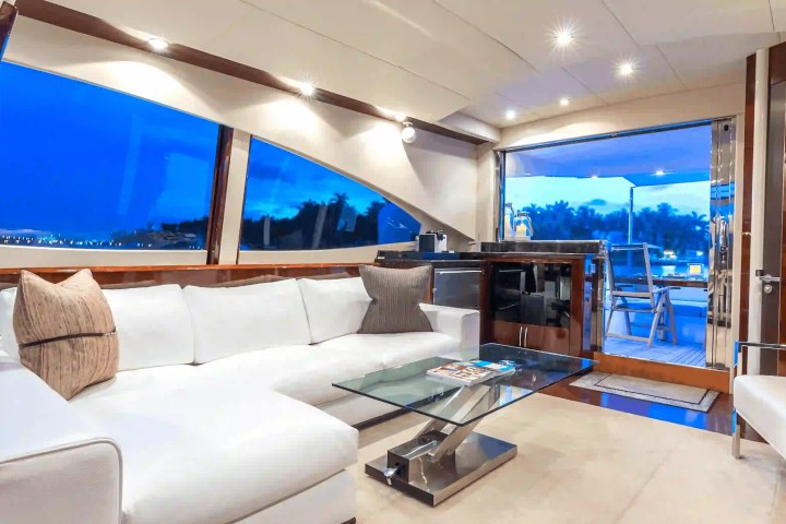Luxurious yacht interior with white sofas, glass table, and large windows showing an ocean view.