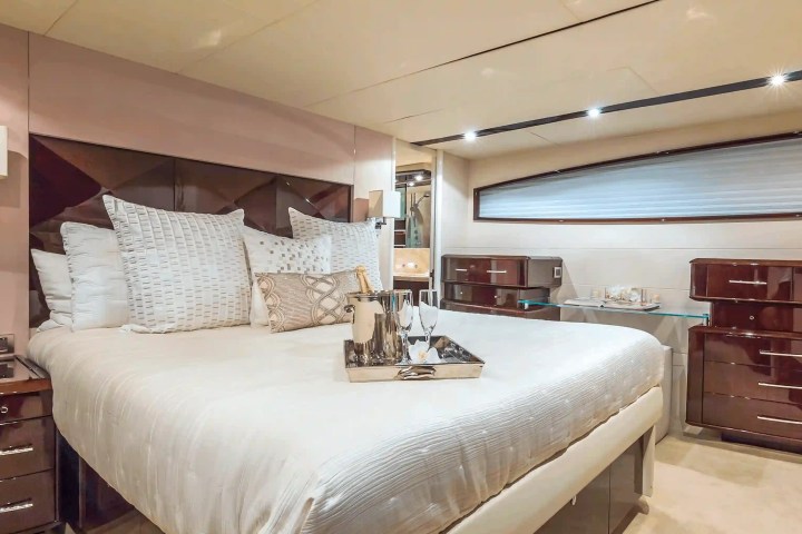 Luxurious yacht bedroom with a neatly arranged bed, nightstands, and a tray with champagne glasses.
