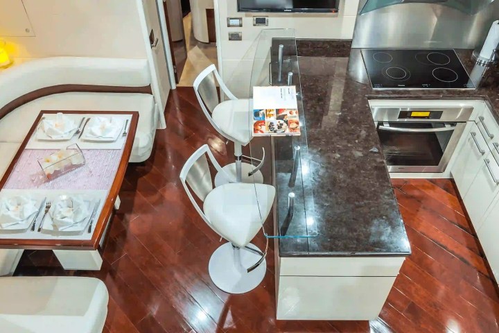 Modern kitchen with bar stools, dining table, and stainless steel appliances on wooden flooring.