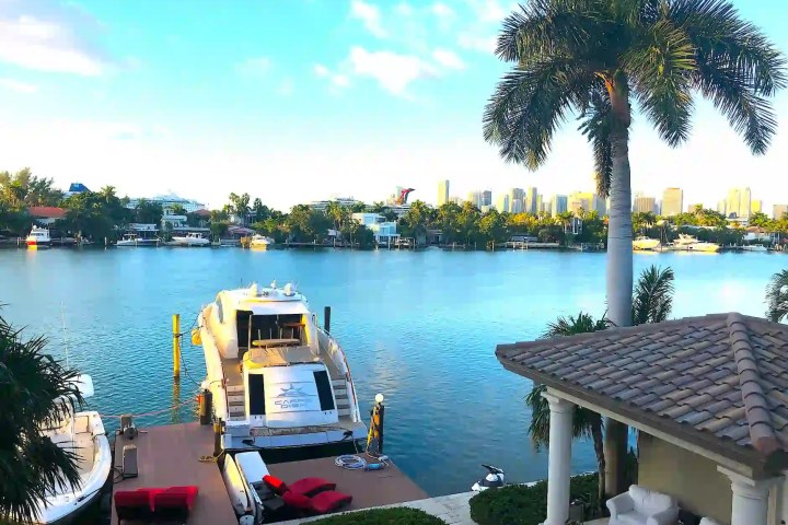A yacht docked on a serene waterfront lined with palm trees and distant city skyline.