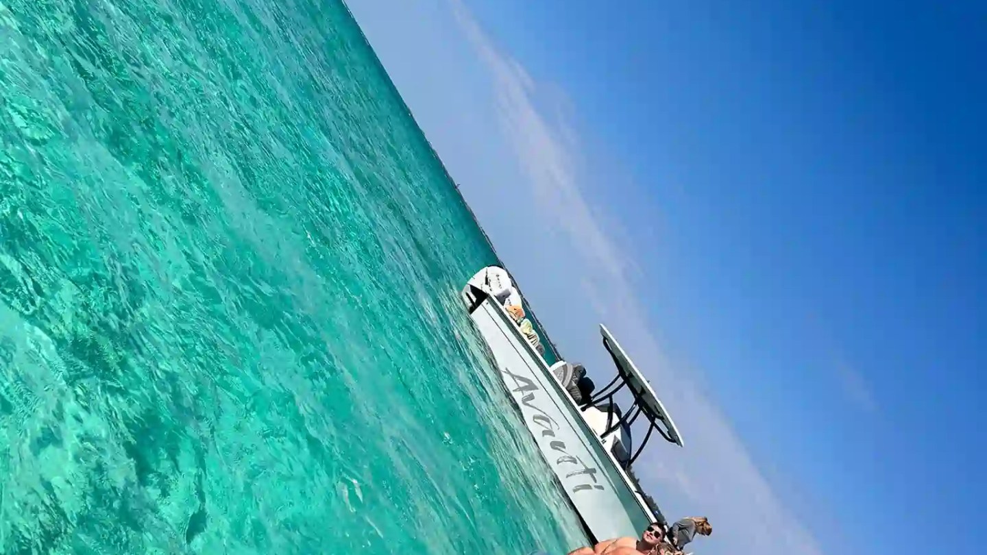 Group on a banana boat in clear turquoise water near a boat under a bright blue sky.