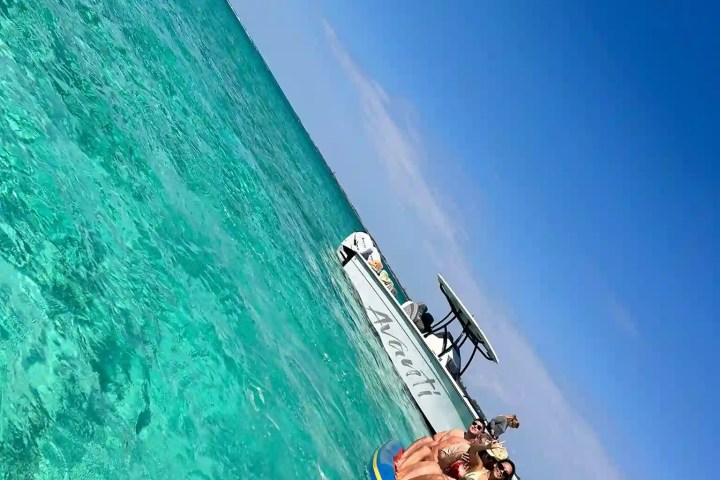 Group on a banana boat in clear turquoise water near a boat under a bright blue sky.