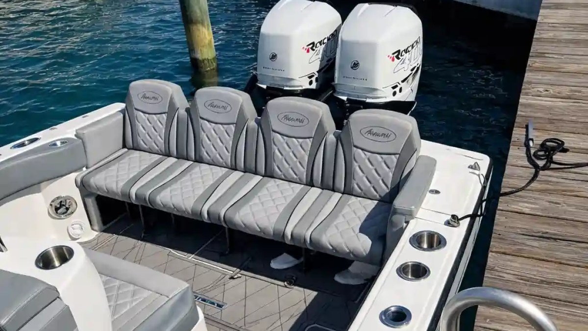 Boat with gray seating and twin engines docked next to a pier.