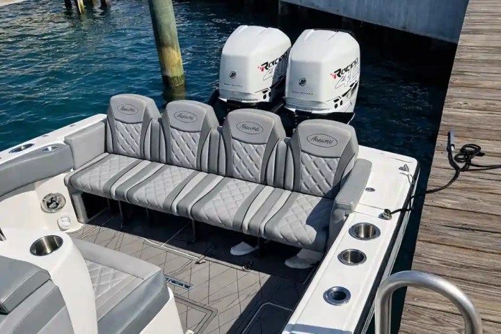 Boat with gray seating and twin engines docked next to a pier.