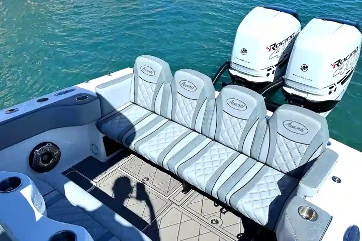 Boat deck with gray seating and dual outboard motors on blue water.