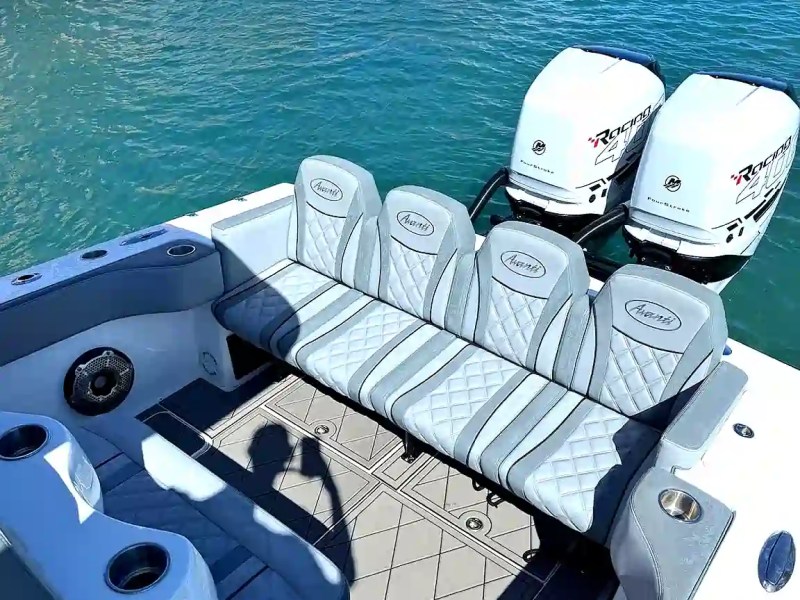 Boat deck with gray seating and dual outboard motors on blue water.
