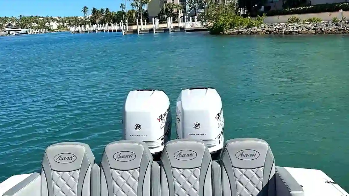 Boat interior with gray seats, twin engines, and a waterfront view of colorful buildings and palm trees.