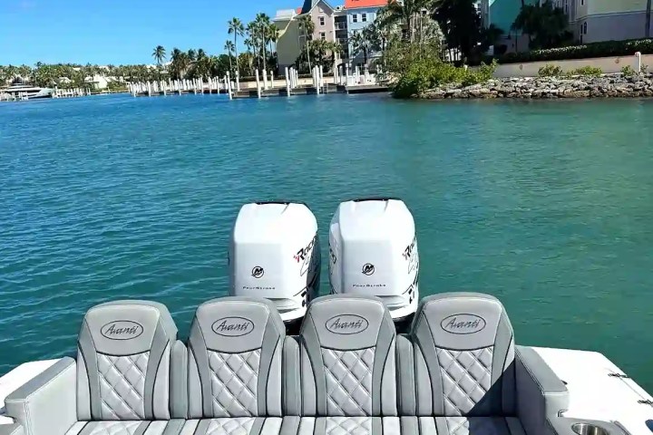 Boat interior with gray seats, twin engines, and a waterfront view of colorful buildings and palm trees.