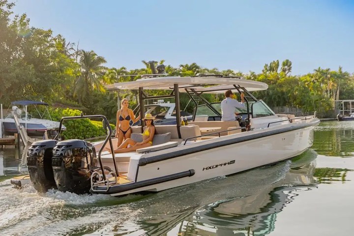 Two people in swimsuits on a boat with a man steering, surrounded by lush greenery.