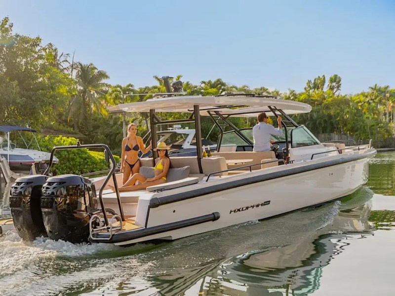 Two people in swimsuits on a boat with a man steering, surrounded by lush greenery.