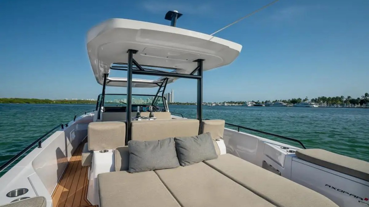 Luxurious boat deck with tan seating and pillows, sailing on a clear blue sea under a sunny sky.