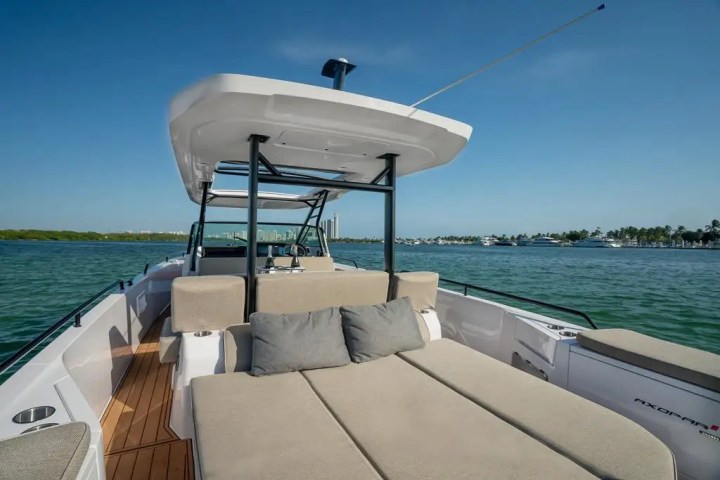 Luxurious boat deck with tan seating and pillows, sailing on a clear blue sea under a sunny sky.