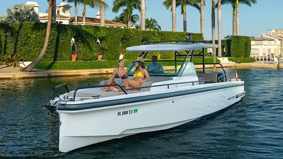 People relaxing on a white motorboat near palm trees and waterfront homes.