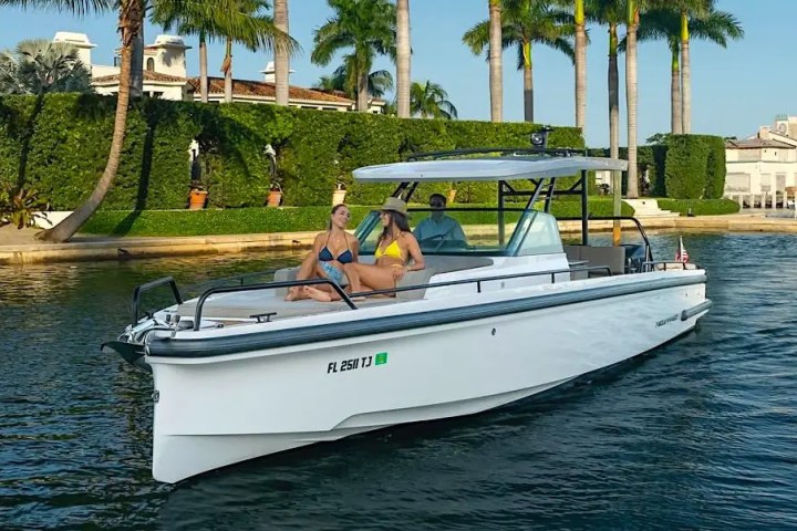 People relaxing on a white motorboat near palm trees and waterfront homes.