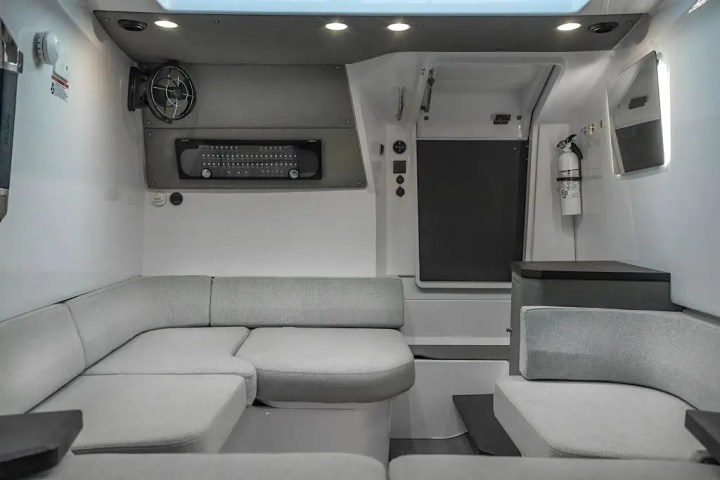 Modern RV interior with gray seating, fan, and fire extinguisher.