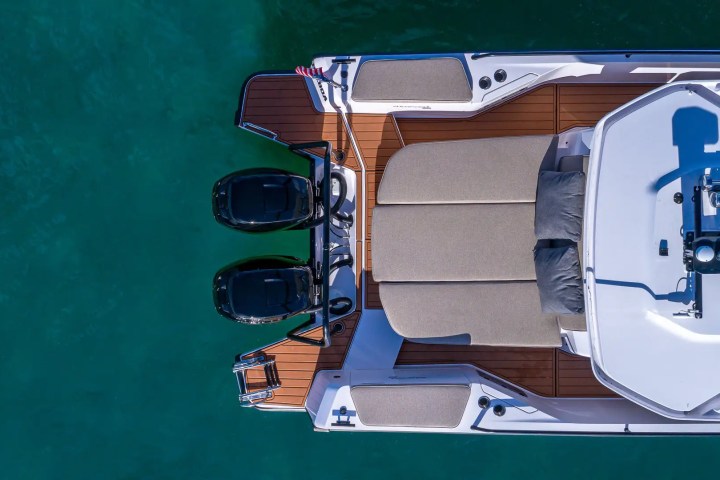 Bird's-eye view of a boat deck with seating and twin outboard motors on green water.