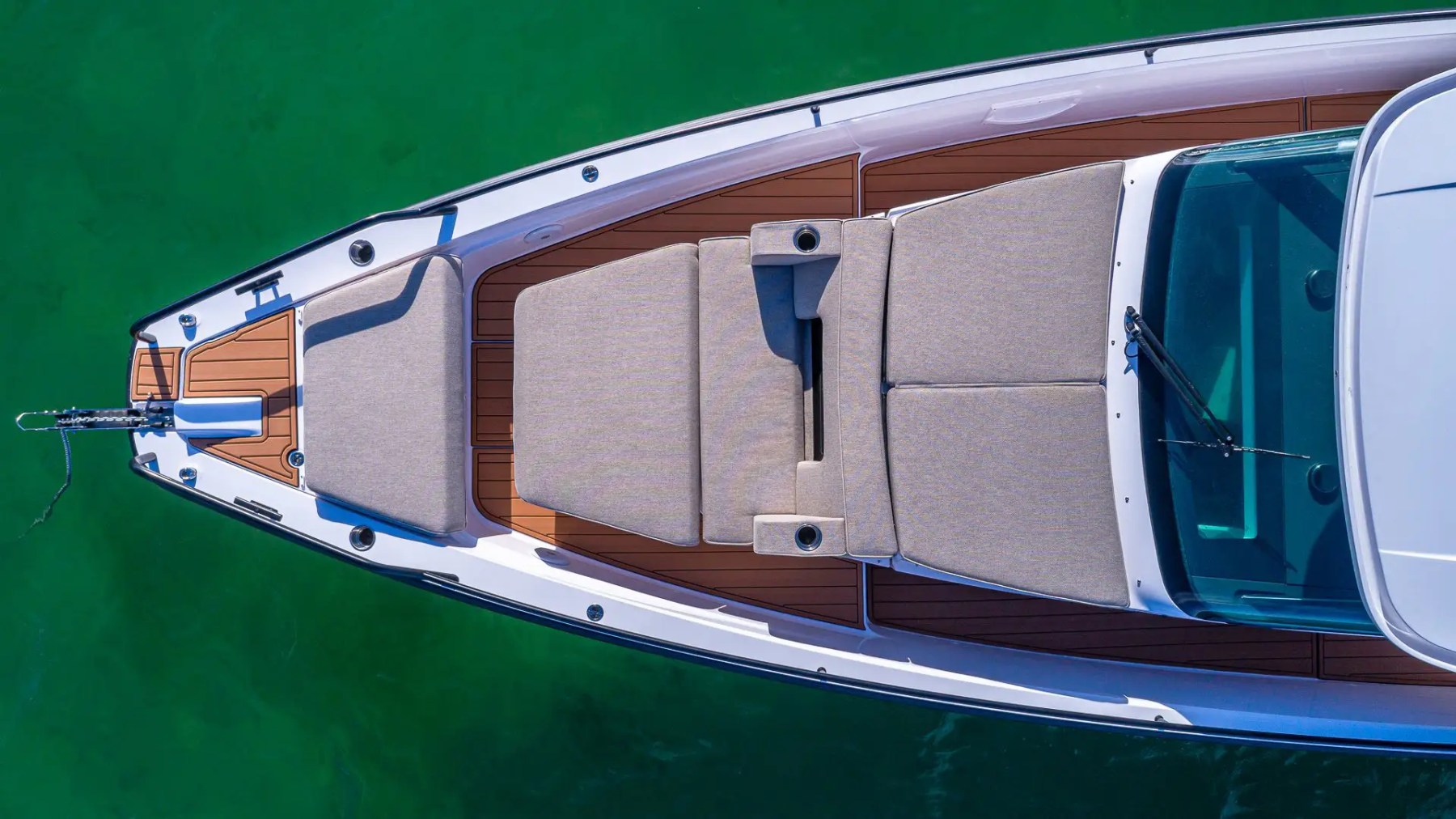 Top view of a boat with beige cushions and wooden deck, floating on green water.