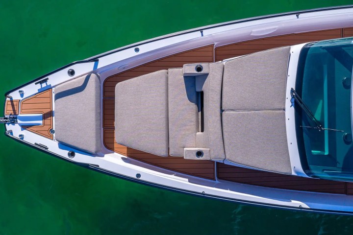 Top view of a boat with beige cushions and wooden deck, floating on green water.