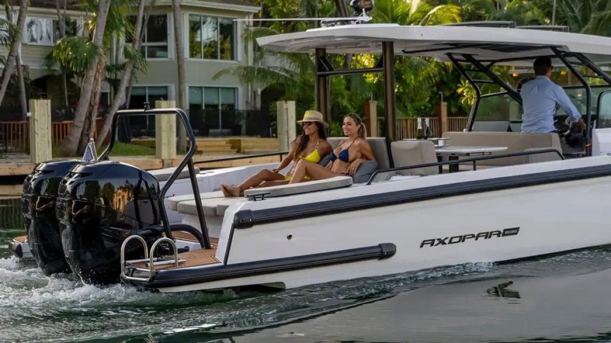 Two women relaxing on a motorboat near a tropical waterfront home.