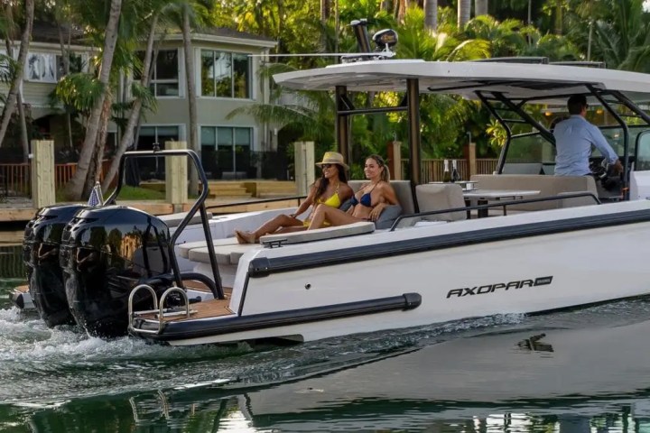 Two women relaxing on a motorboat near a tropical waterfront home.