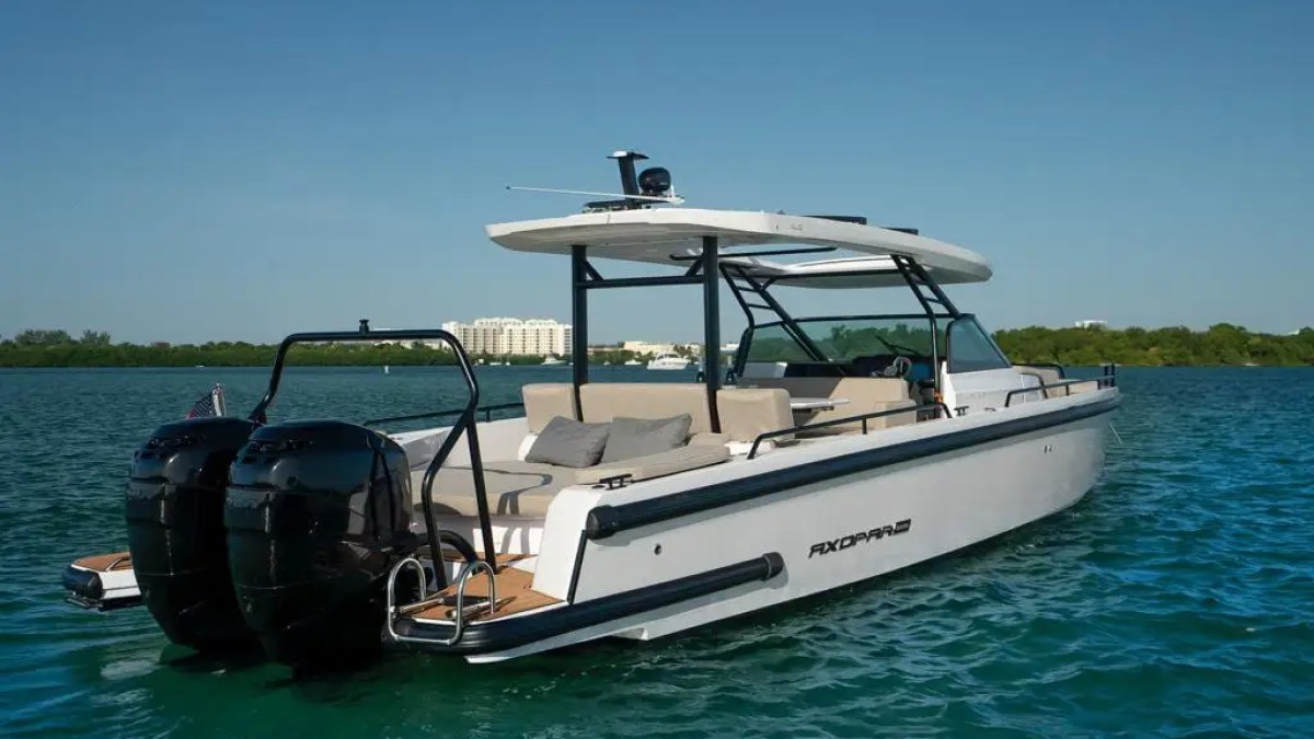 A sleek motorboat with dual engines on a lake under a clear blue sky.
