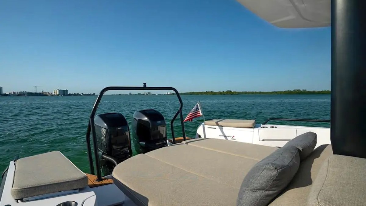 Boat deck with seating and two engines, American flag, water and distant shoreline.