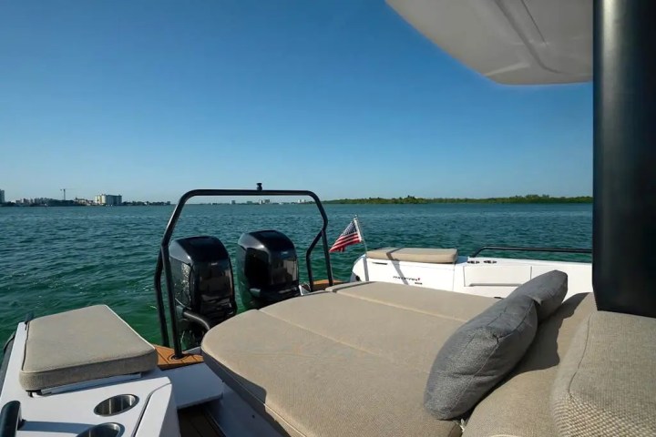 Boat deck with seating and two engines, American flag, water and distant shoreline.
