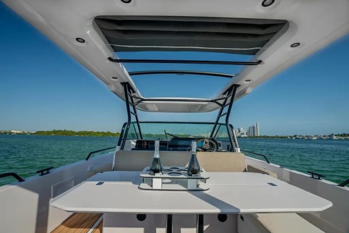 View from a boat's seating area with a table and bottle, overlooking a calm sea and city skyline.