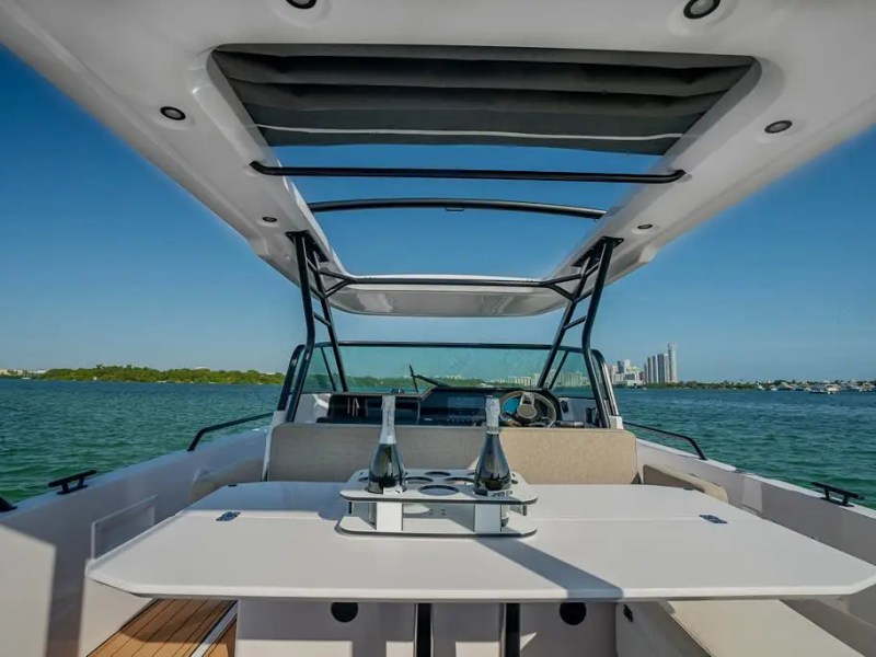 View from a boat's seating area with a table and bottle, overlooking a calm sea and city skyline.