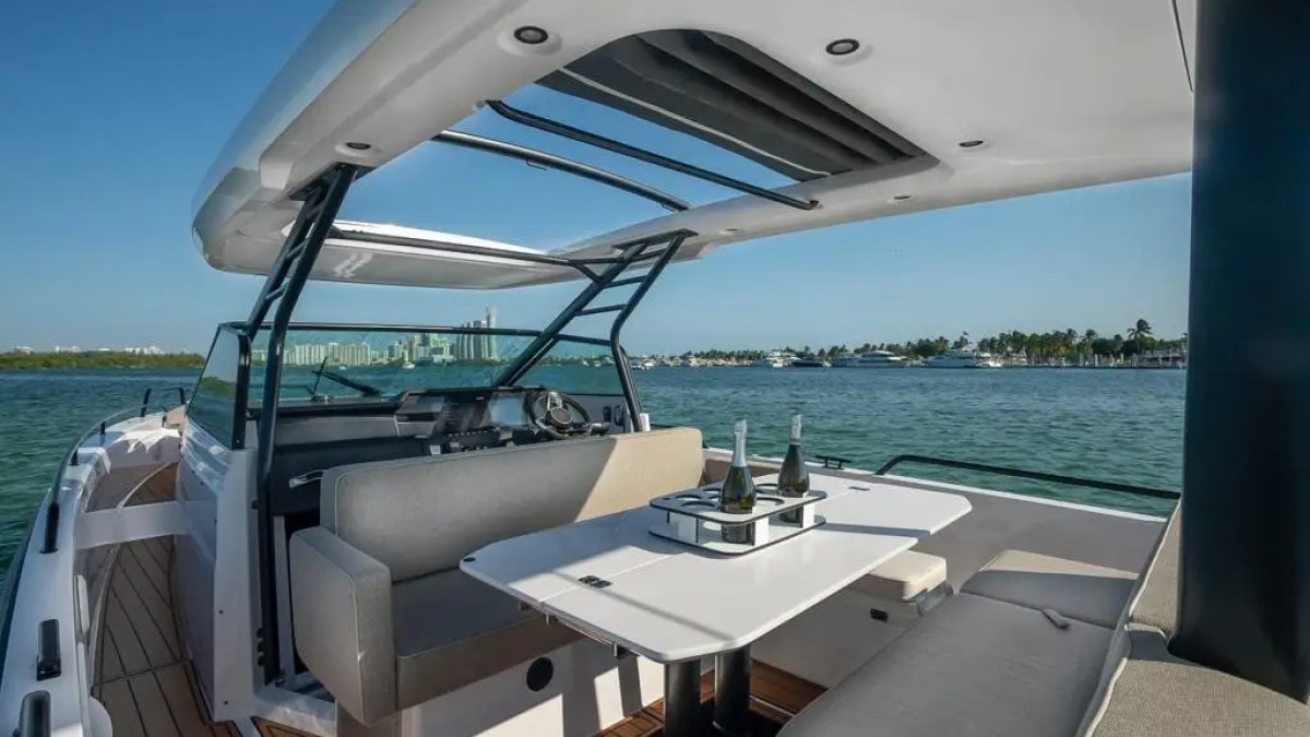 Luxury boat deck with seating area, table, and champagne bottles, overlooking a scenic waterfront view.