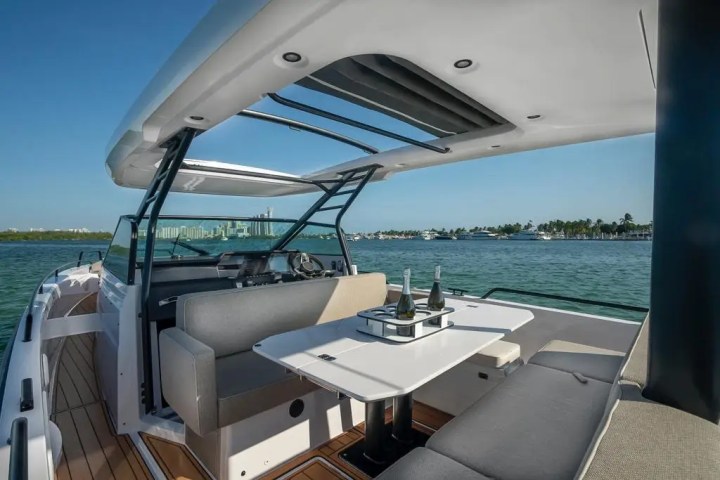 Luxury boat deck with seating area, table, and champagne bottles, overlooking a scenic waterfront view.