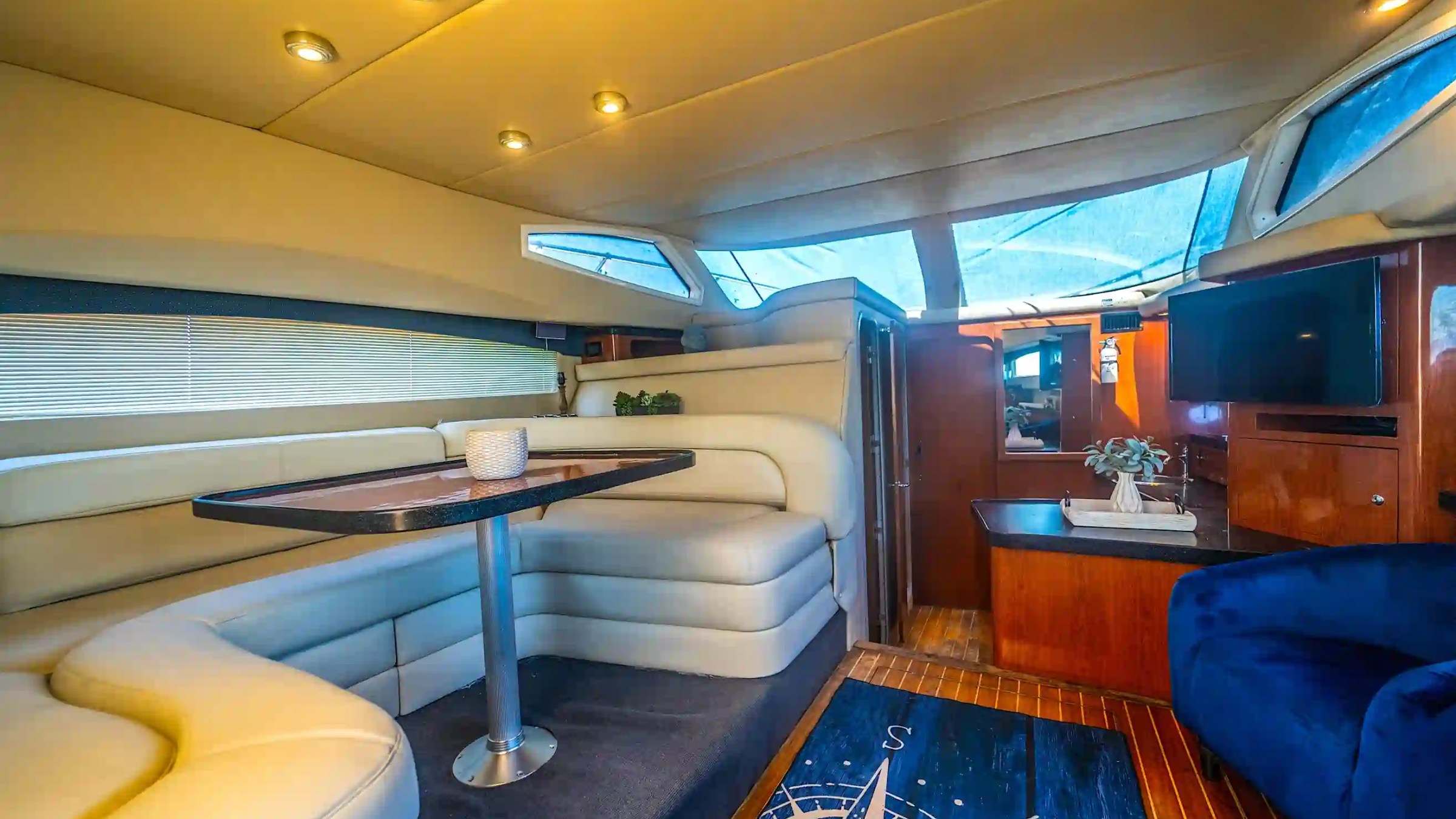 Interior of a luxury yacht with sofa, table, TV, and skylight windows.