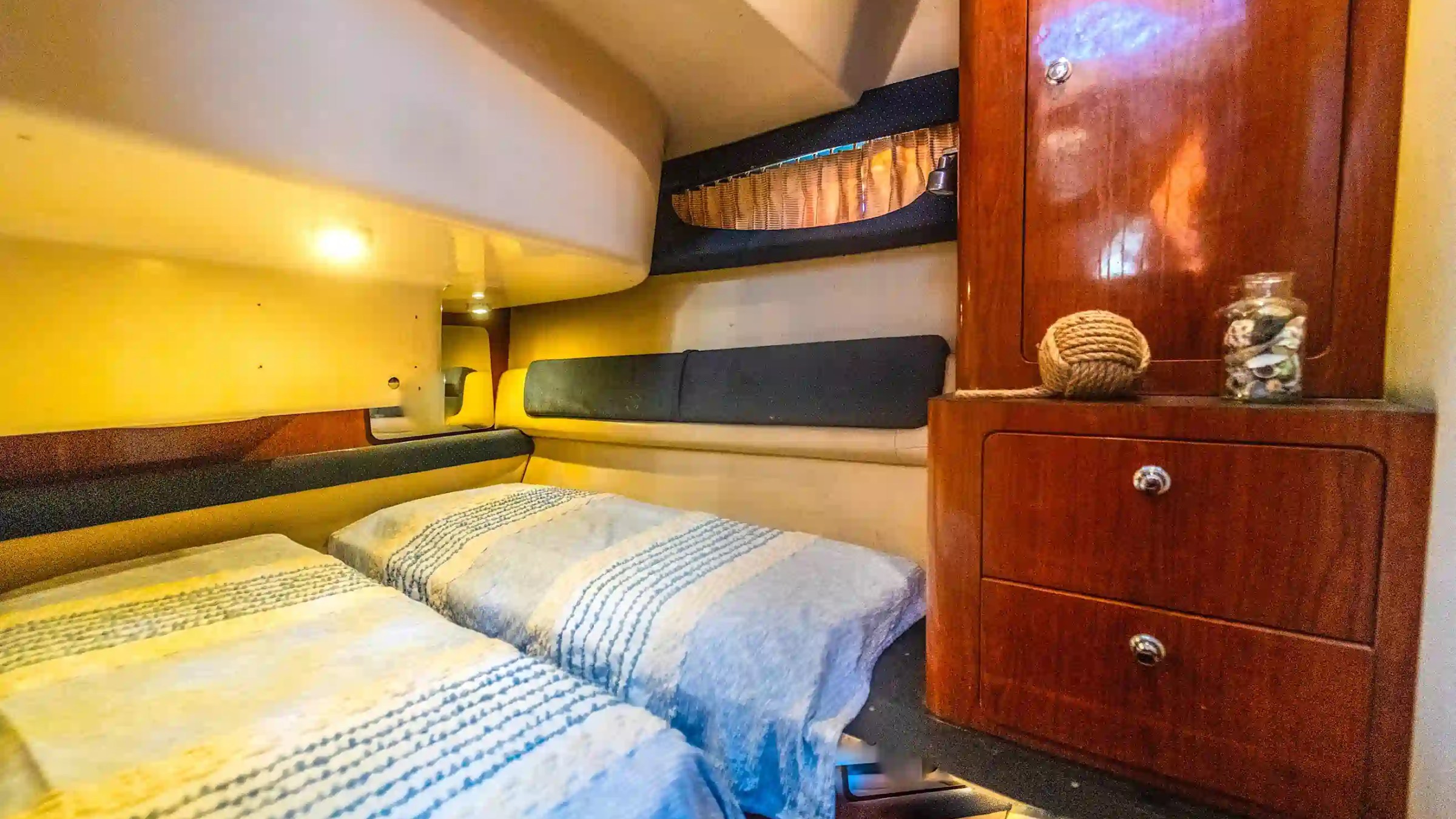 Cozy boat cabin with twin beds, wooden cabinet, and nautical decor.