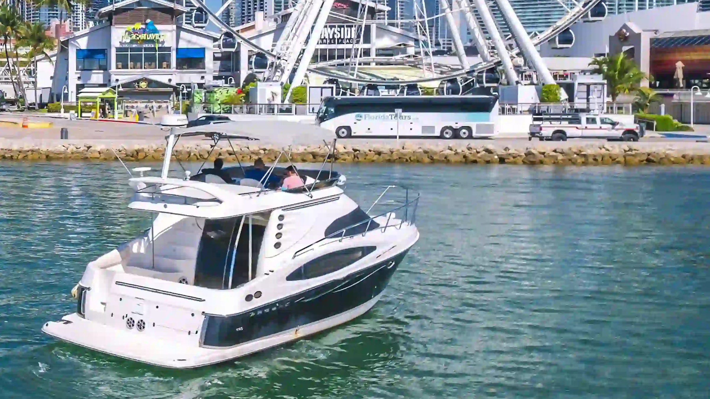 A boat on water near a waterfront Ferris wheel and buildings.