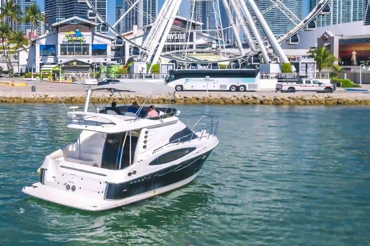 A boat on water near a waterfront Ferris wheel and buildings.