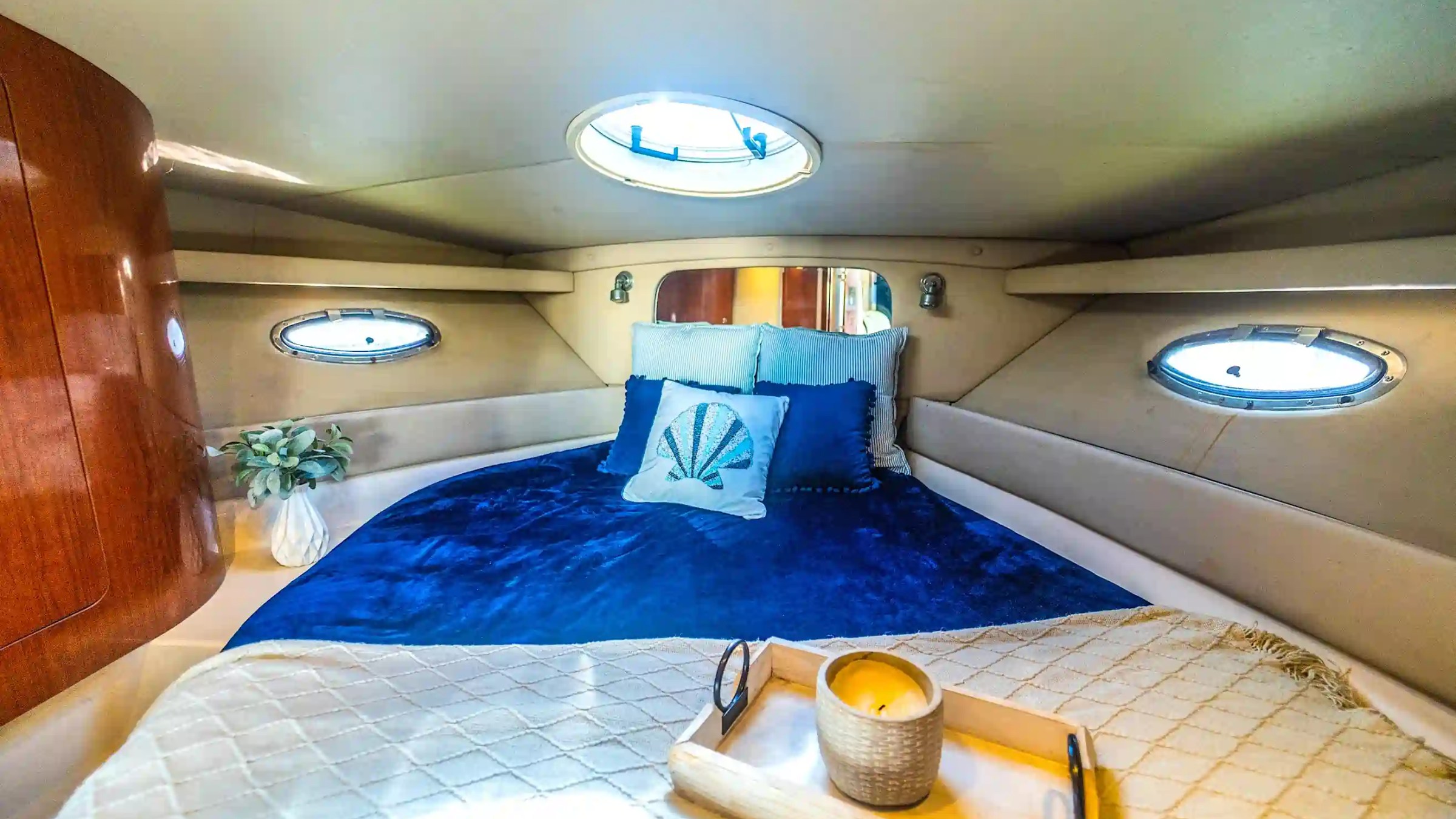 Cozy boat cabin with blue bedding, decorative pillows, and tray with a candle.