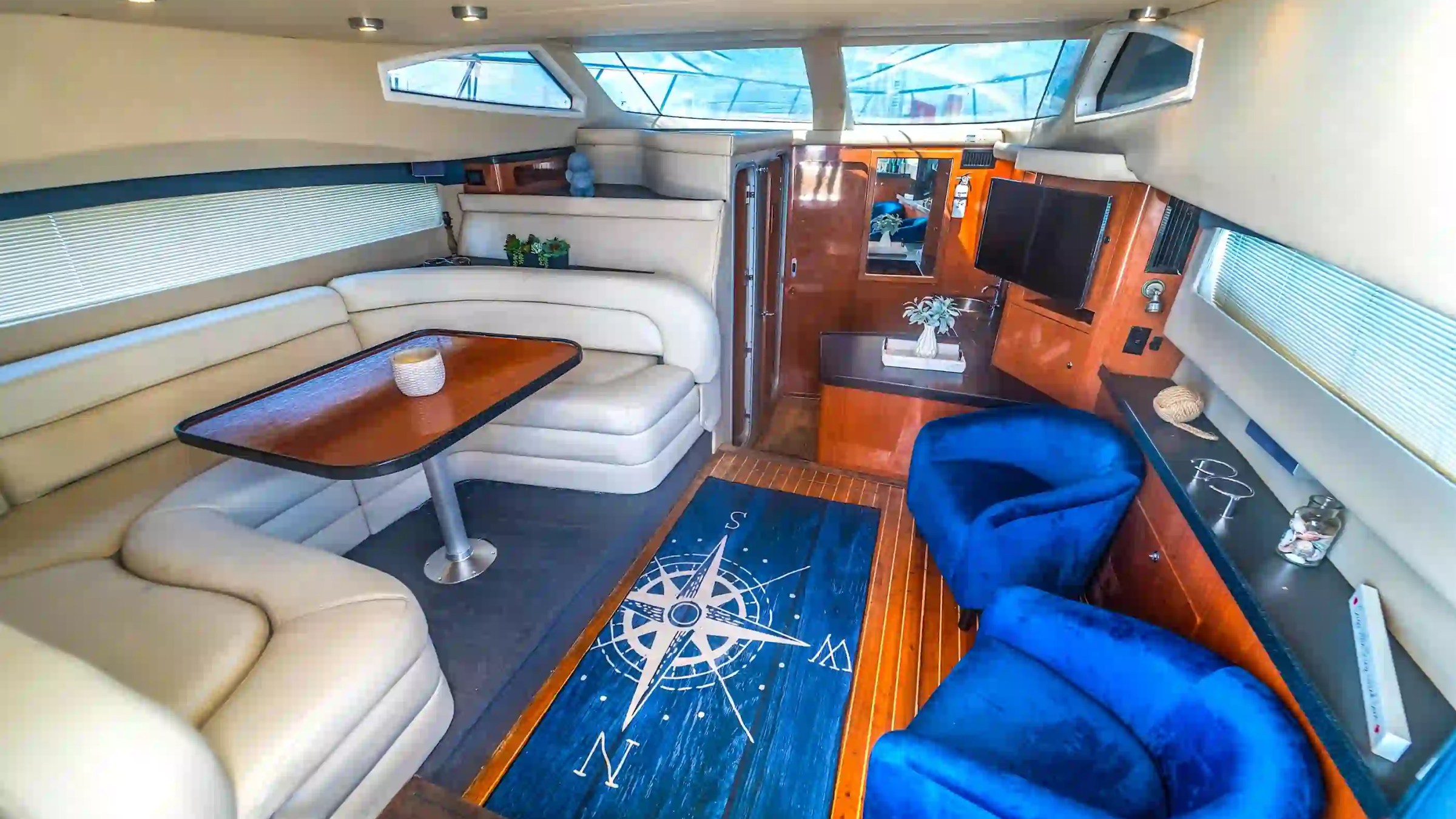 Interior of a yacht with white seating, blue chairs, compass rug, and a small TV.