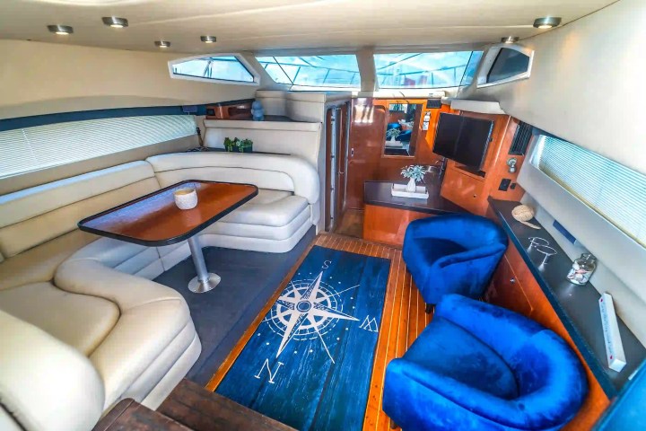 Interior of a yacht with white seating, blue chairs, compass rug, and a small TV.