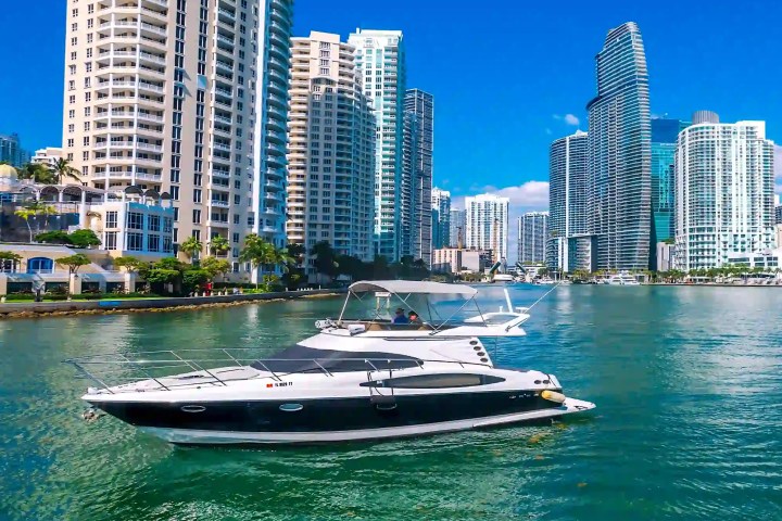 Boat on water with city skyscrapers and blue sky in the background.