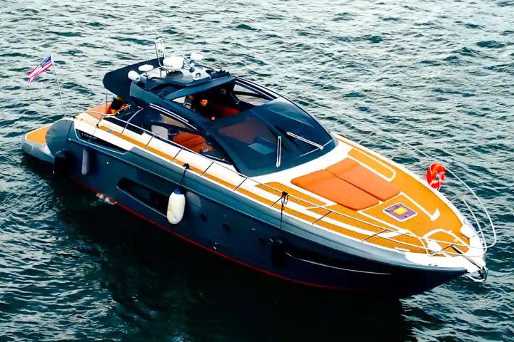 A sleek, modern yacht with orange accents floating on the water, with a flag at the rear.