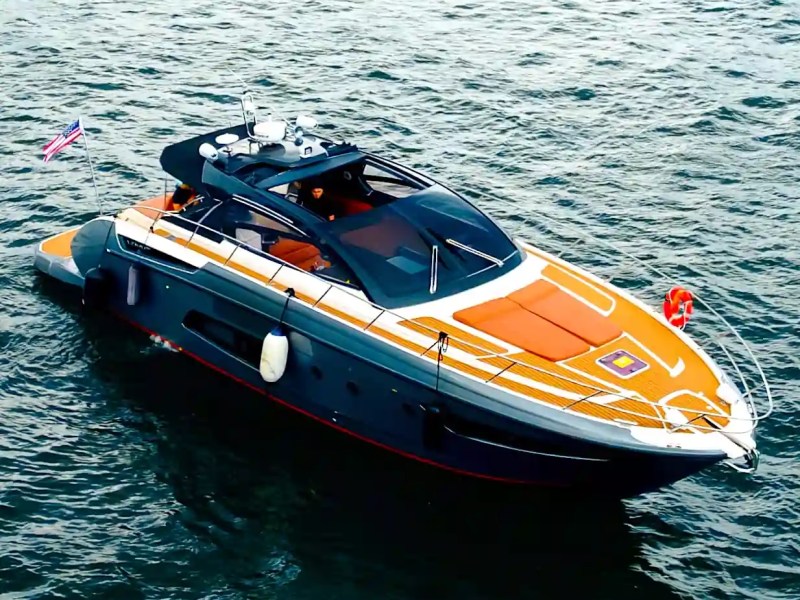 A sleek, modern yacht with orange accents floating on the water, with a flag at the rear.