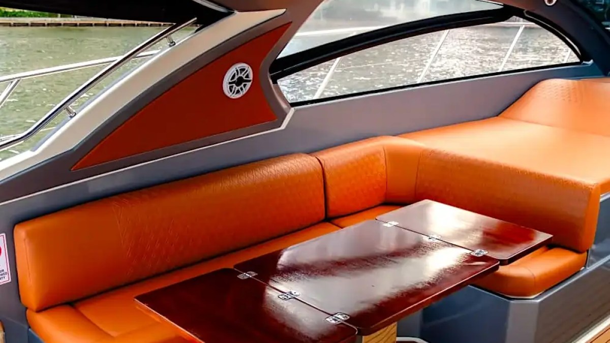 Orange seating area on a boat with a wooden table and large windows.