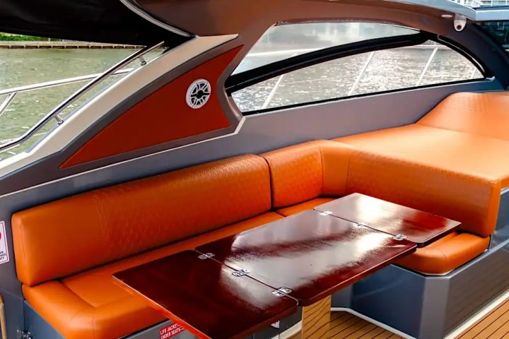 Orange seating area on a boat with a wooden table and large windows.