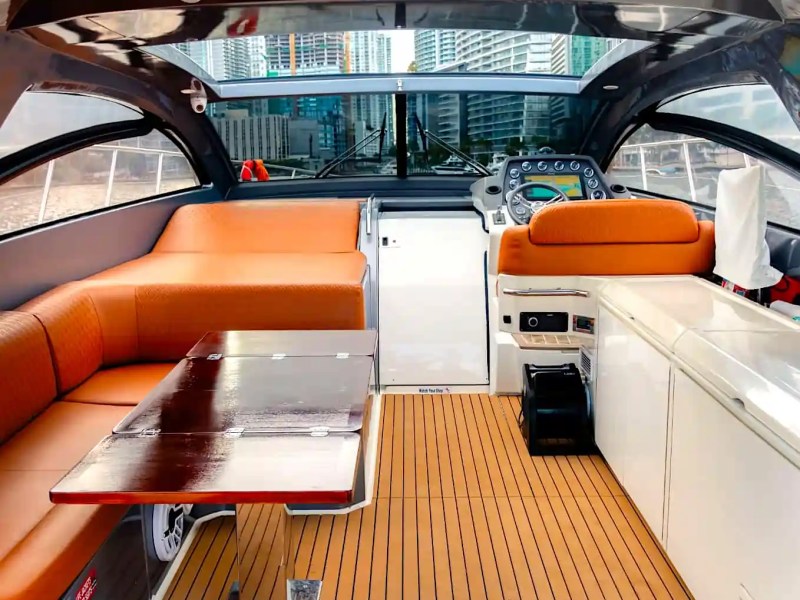 Interior of a yacht with orange seating, wooden table, and view of city skyline through windows.