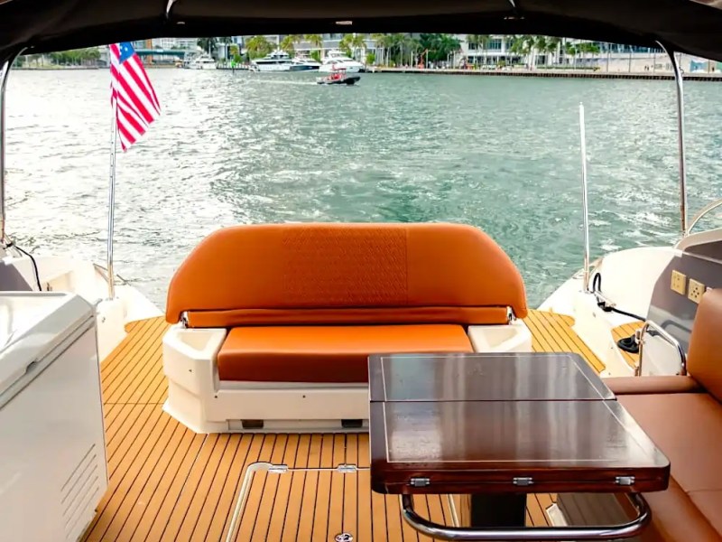 View from yacht's deck with orange seating, wooden table, and flag overlooking the water.