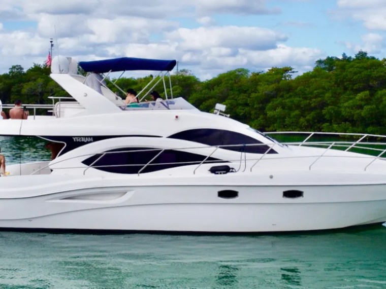 White yacht with blue canopy on calm water near lush green trees.