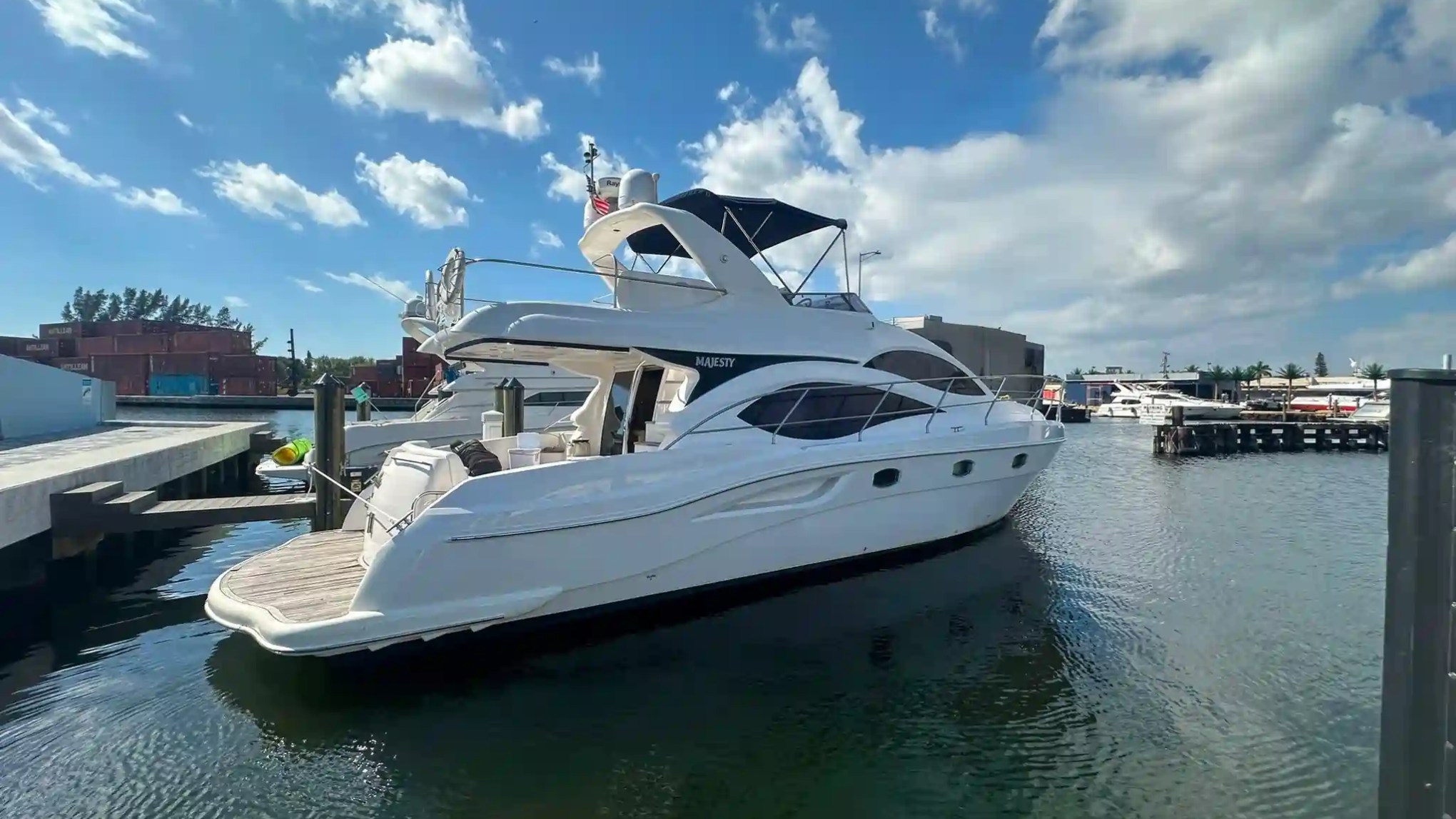 White yacht docked in marina under a partly cloudy blue sky.