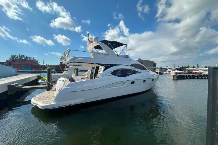 White yacht docked in marina under a partly cloudy blue sky.